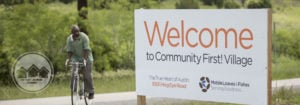 man riding bike next to sign that says Welcome to Community First! Village