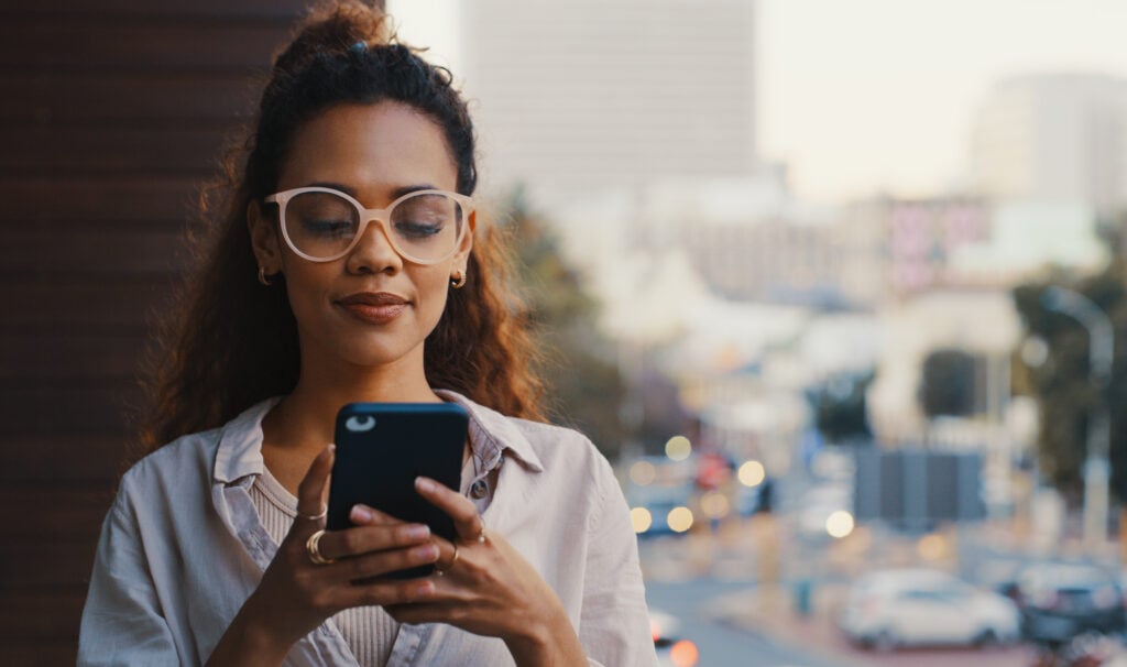 woman on a balcony looking at her phone with a city background